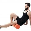 Athlete massaging and stretching legs calf muscles with foam roller. Full body length portrait isolated on white studio background.